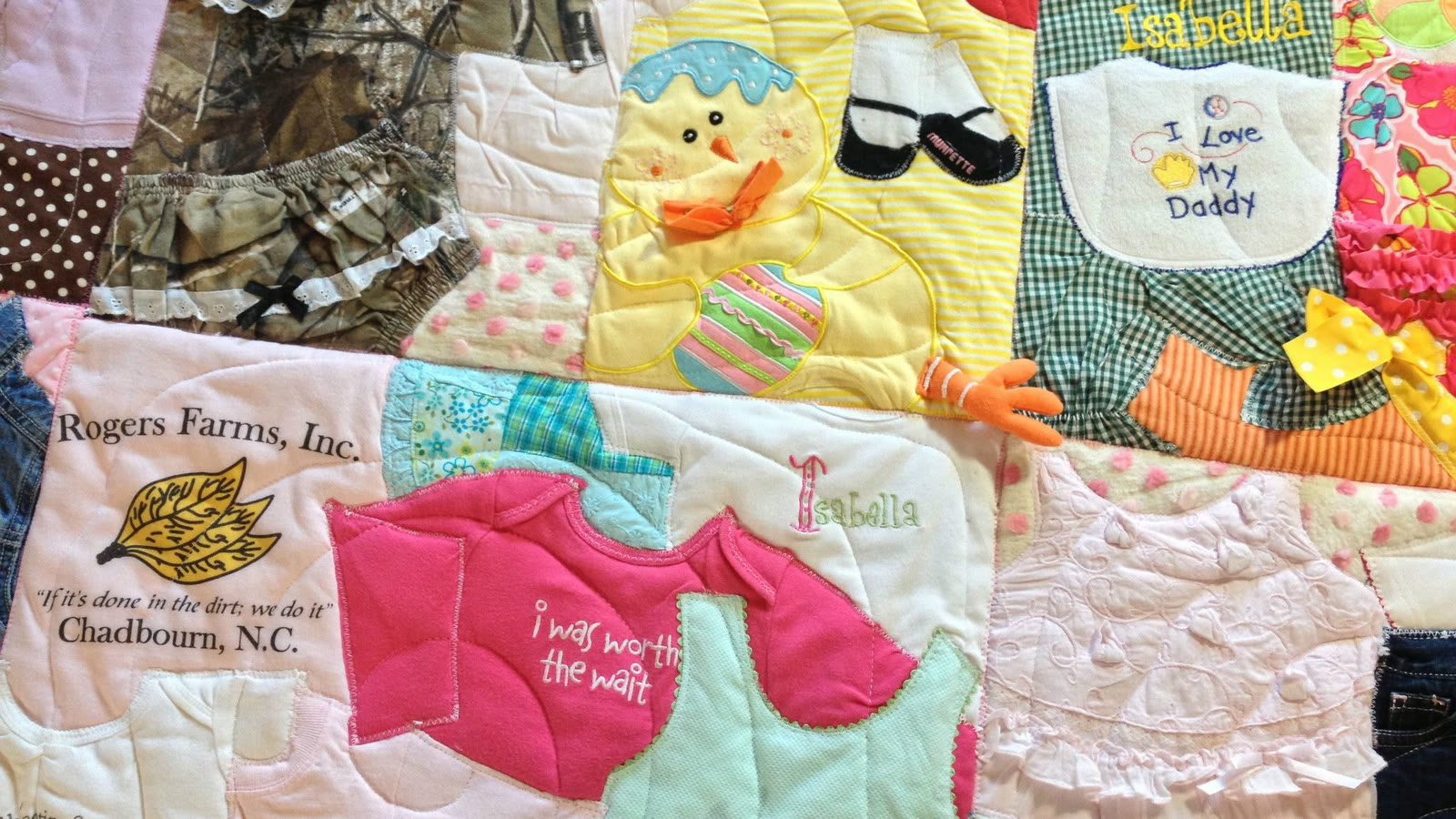 A memory quilt sewn from a baby's outgrown clothes — bibs, onesies and a patch reading 'i was worth the wait'.